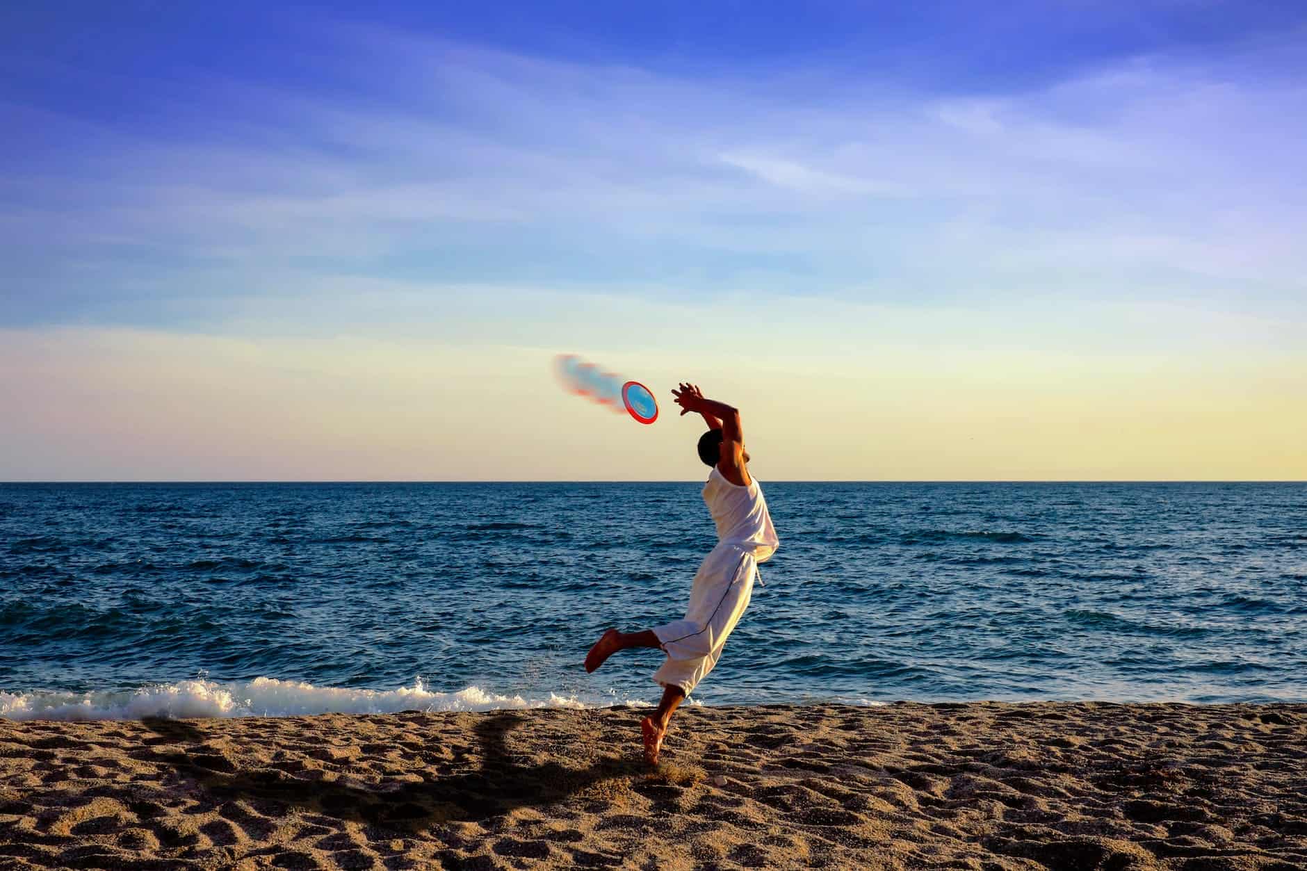 man jumping for frisbee on the beach